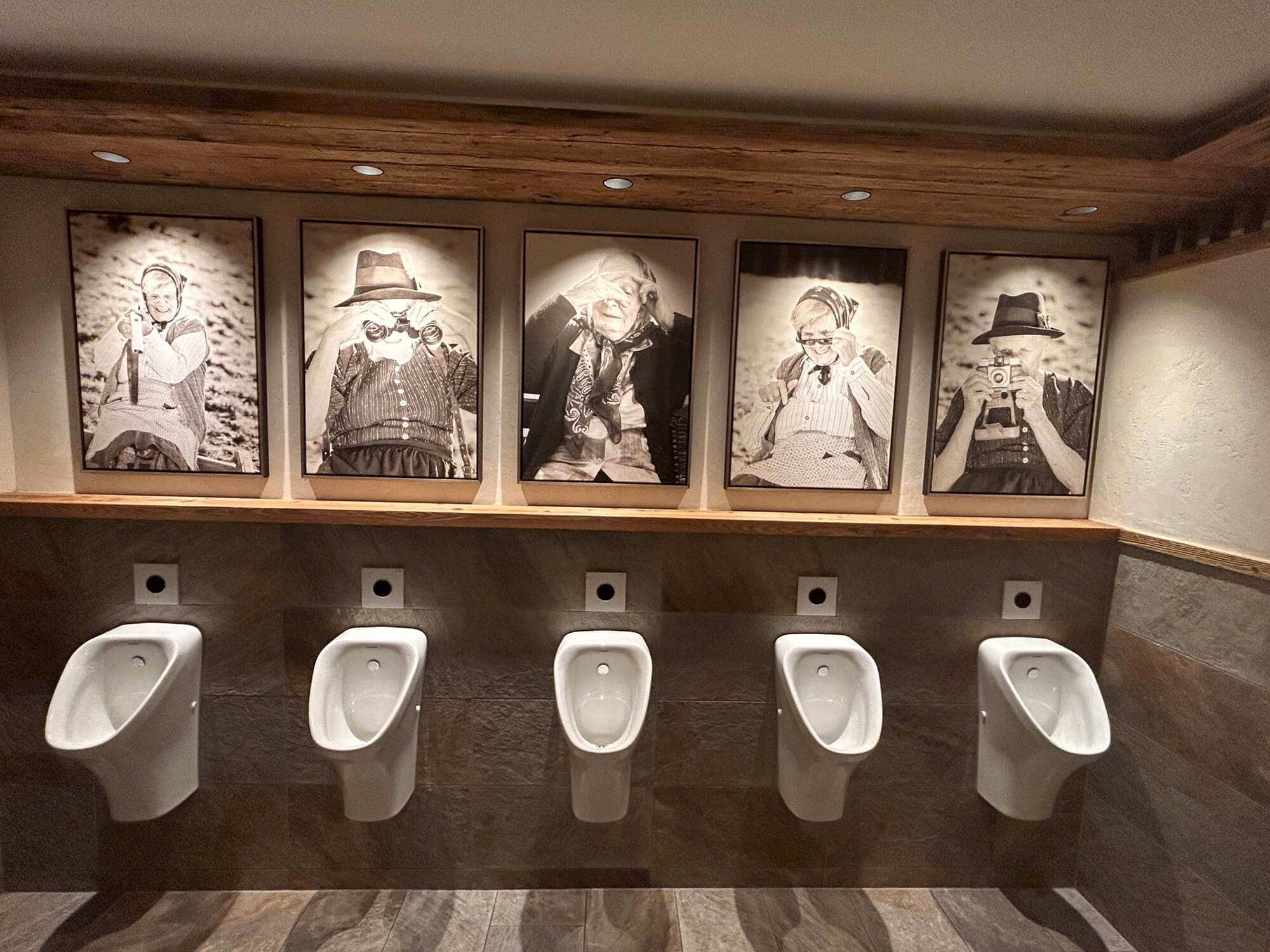 Fünf Urinale unter Schwarz-Weiß-Fotos von Menschen mit Kameras und Ferngläsern.