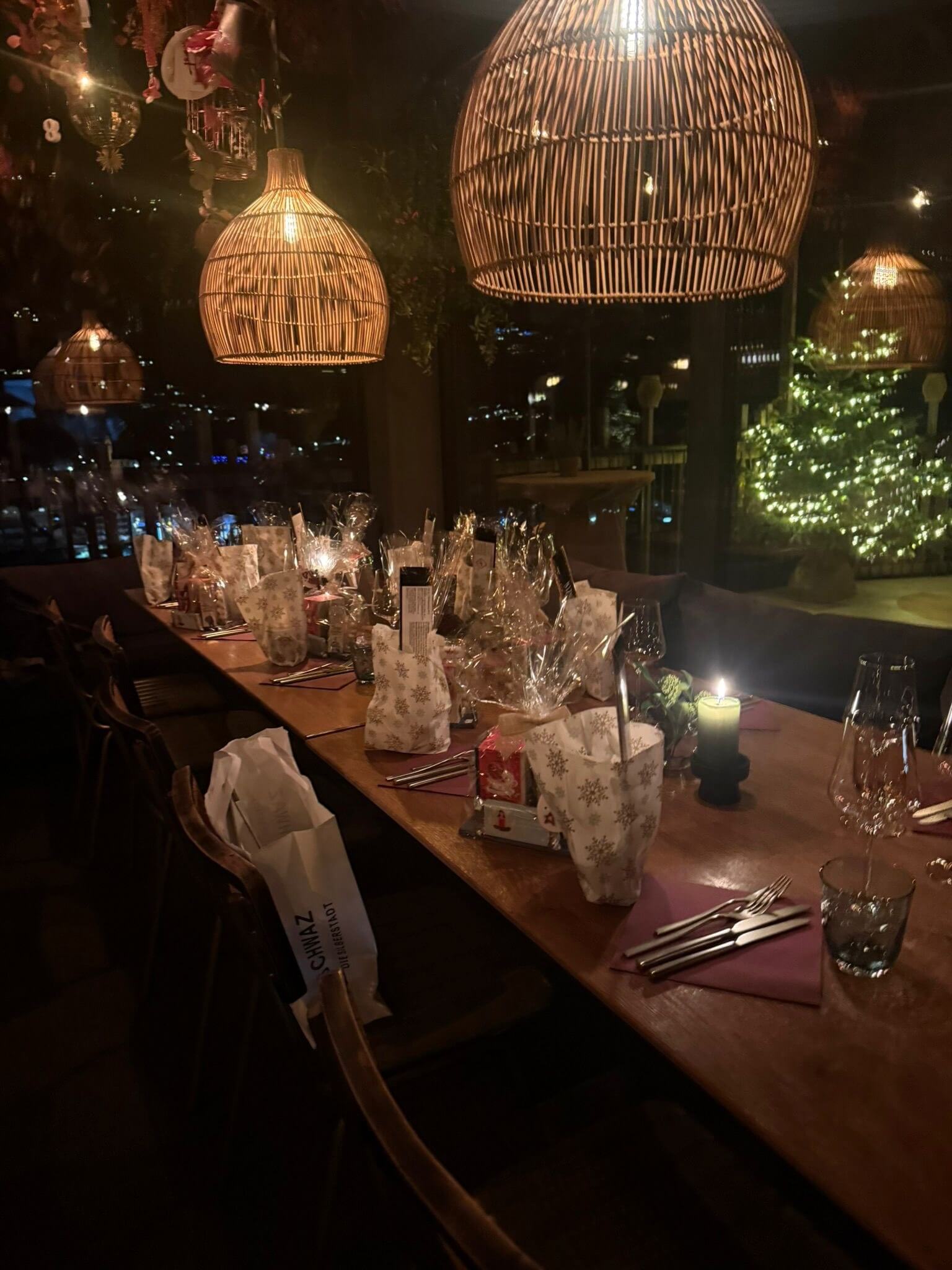 Festlich gedeckte Tafel mit eingepackten Geschenken an jedem Platz, dahinter ein beleuchteter Christbaum.