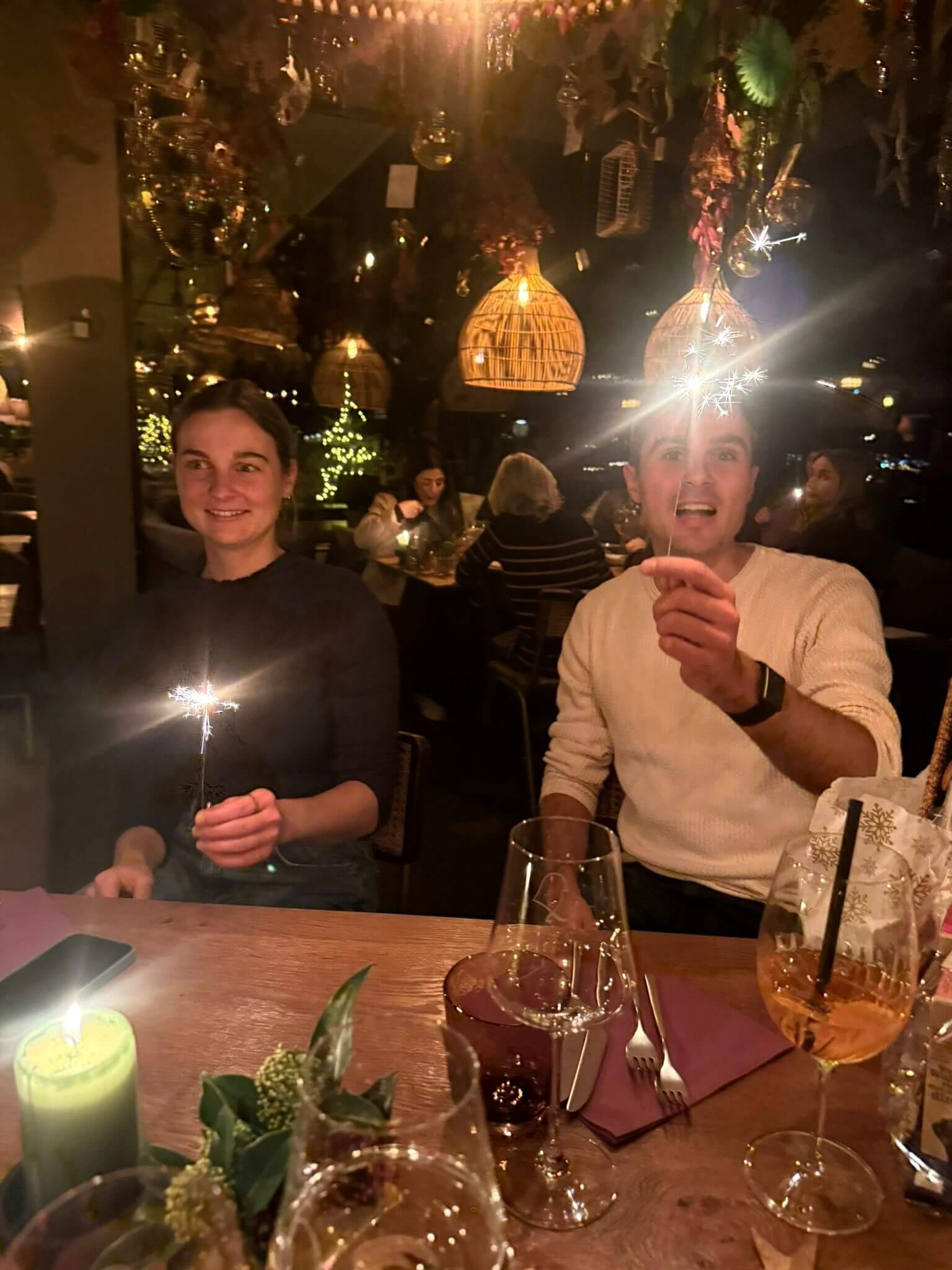 Zwei Teammitglieder halten Wunderkerzen über den Tisch, darüber hängen Korblampen und Weihnachtsschmuck.