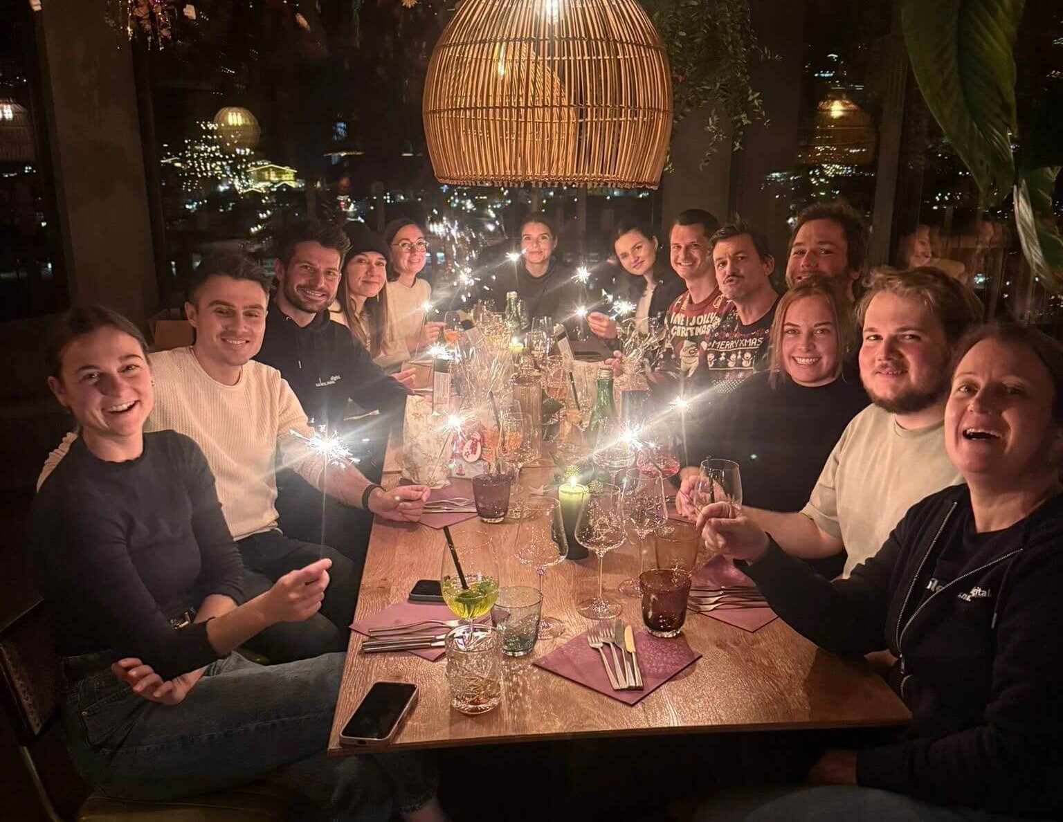 Die KLIXPERT-Runde mit Wunderkerzen an der festlich gedeckten Tafel unter einer Korblampe, im Hintergrund die nächtliche Stadt.