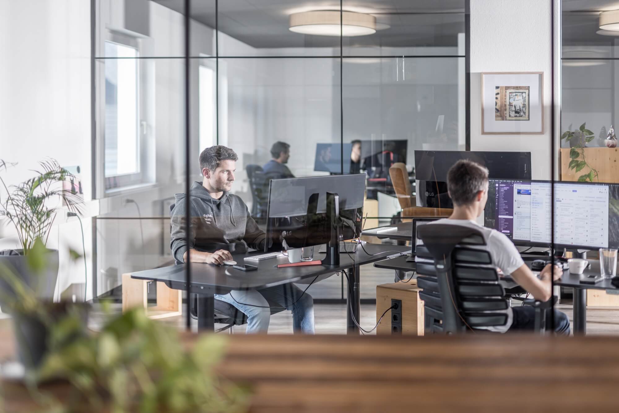 Männer arbeiten an Computern in modernem Büro mit Glaswänden.