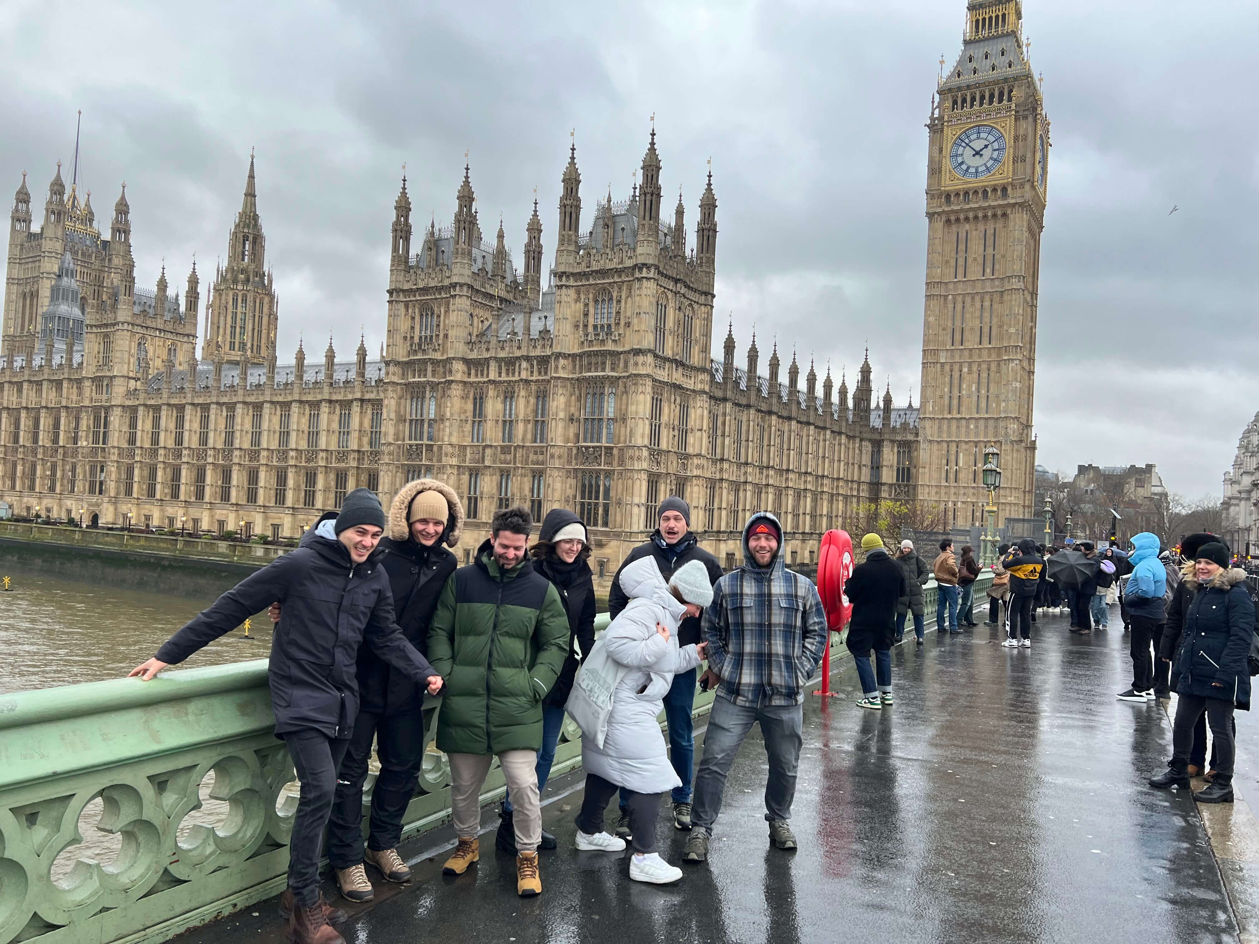 Gruppe von Menschen posiert vor dem Palace of Westminster und Big Ben in London an einem bewölkten Tag.