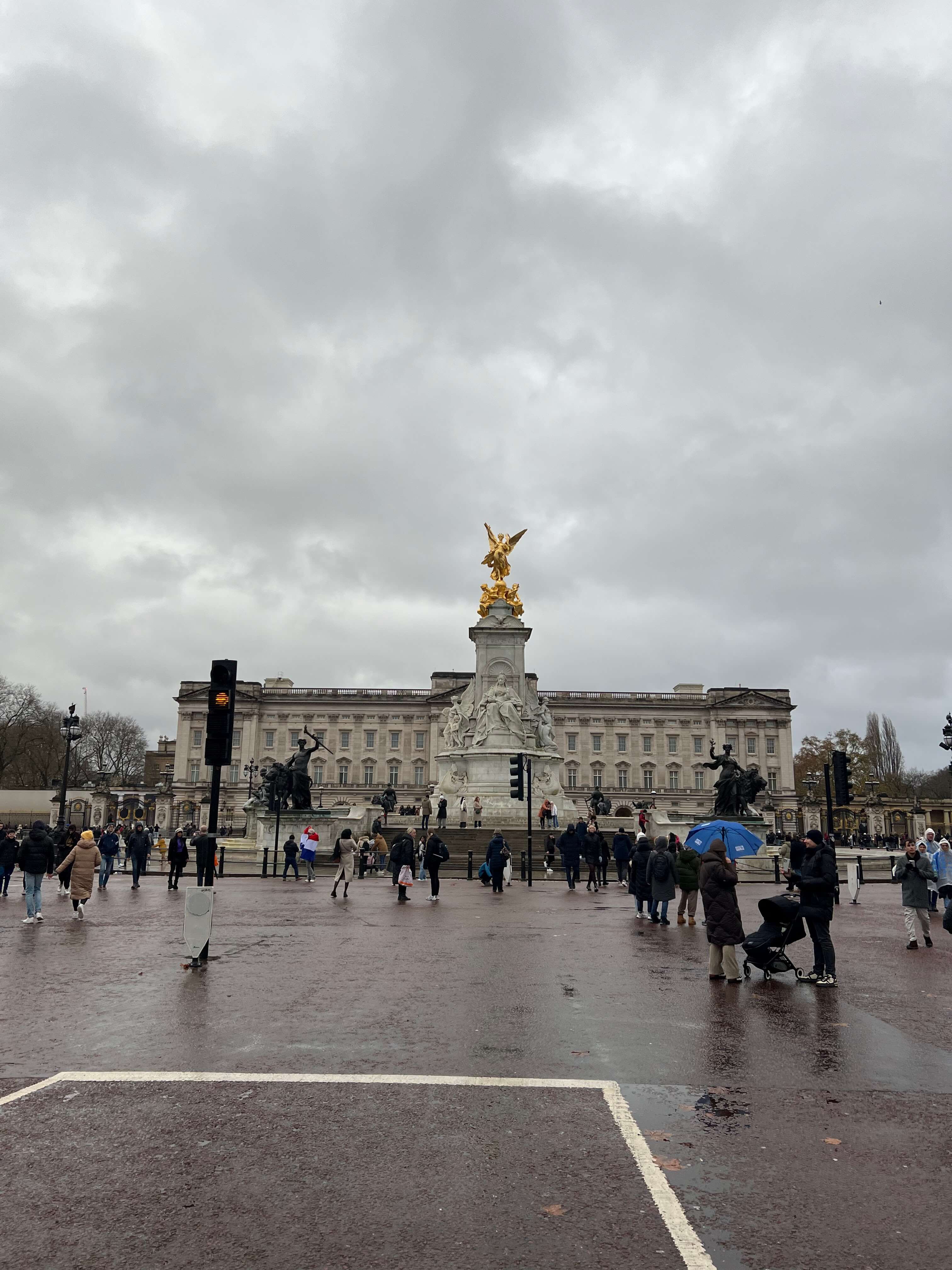 Buckingham Palace bei bewölktem Himmel, Menschen stehen vor dem Victoria Memorial.