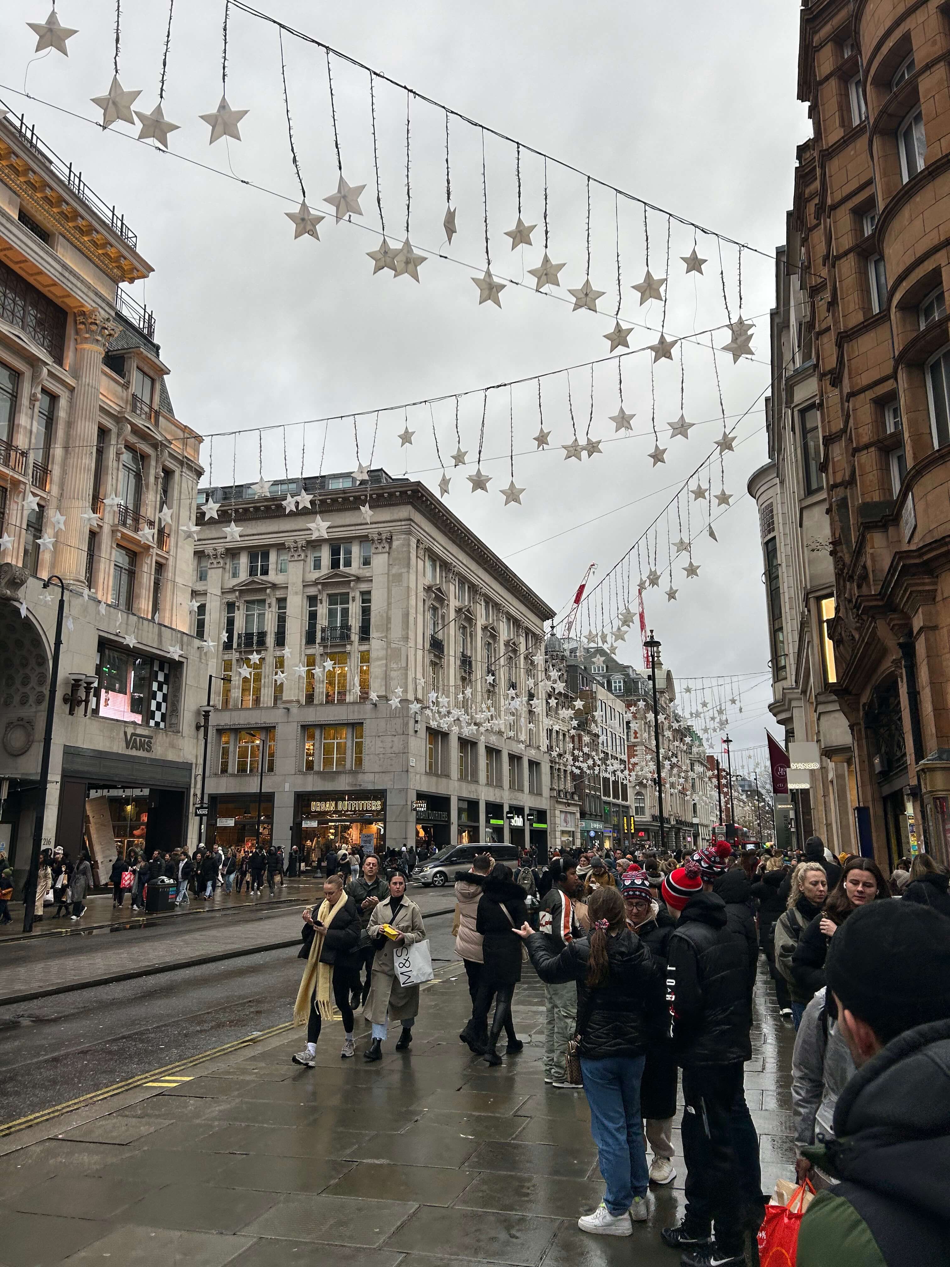 Belebte Einkaufsstraße mit Weihnachtsdekoration in Form von Sternen, viele Menschen beim Einkaufen und Flanieren.