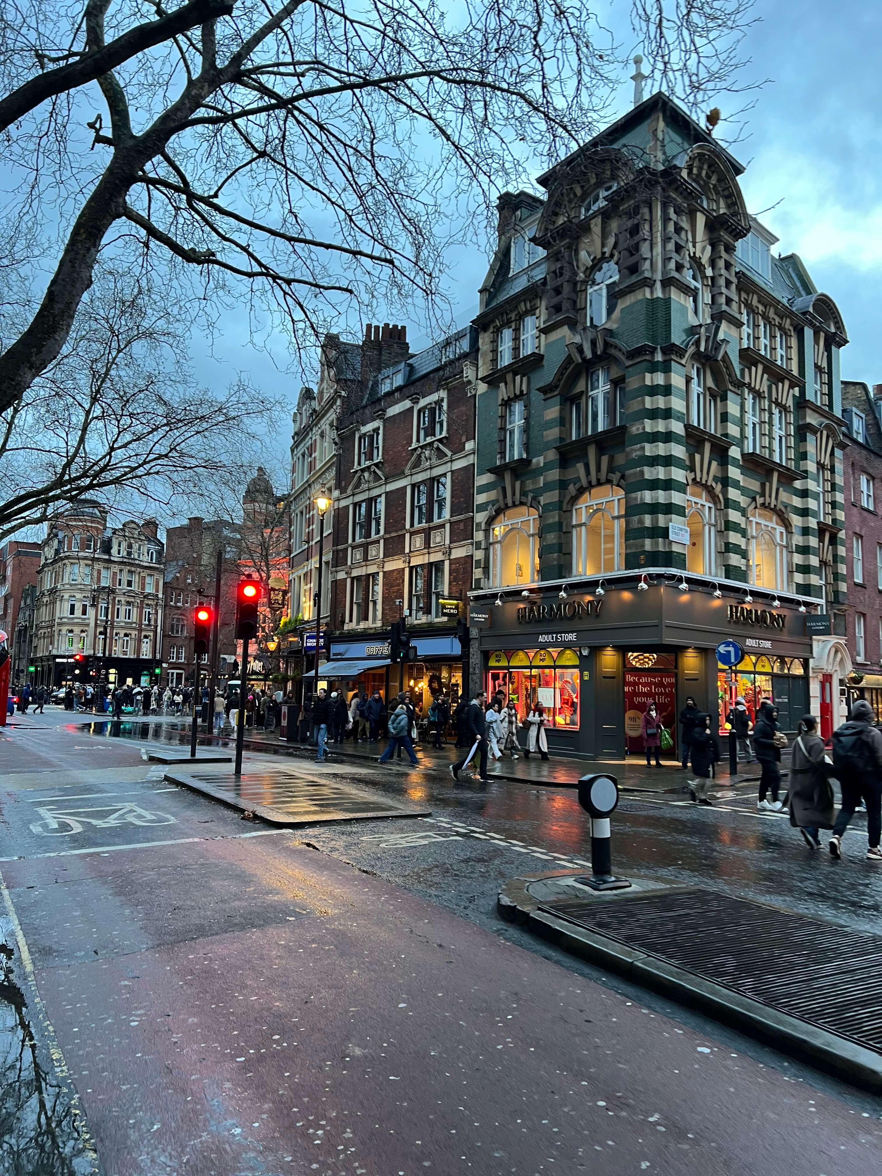 Straßenszene in London mit historischem Gebäude, beleuchteten Geschäften und Passanten bei Dämmerung.