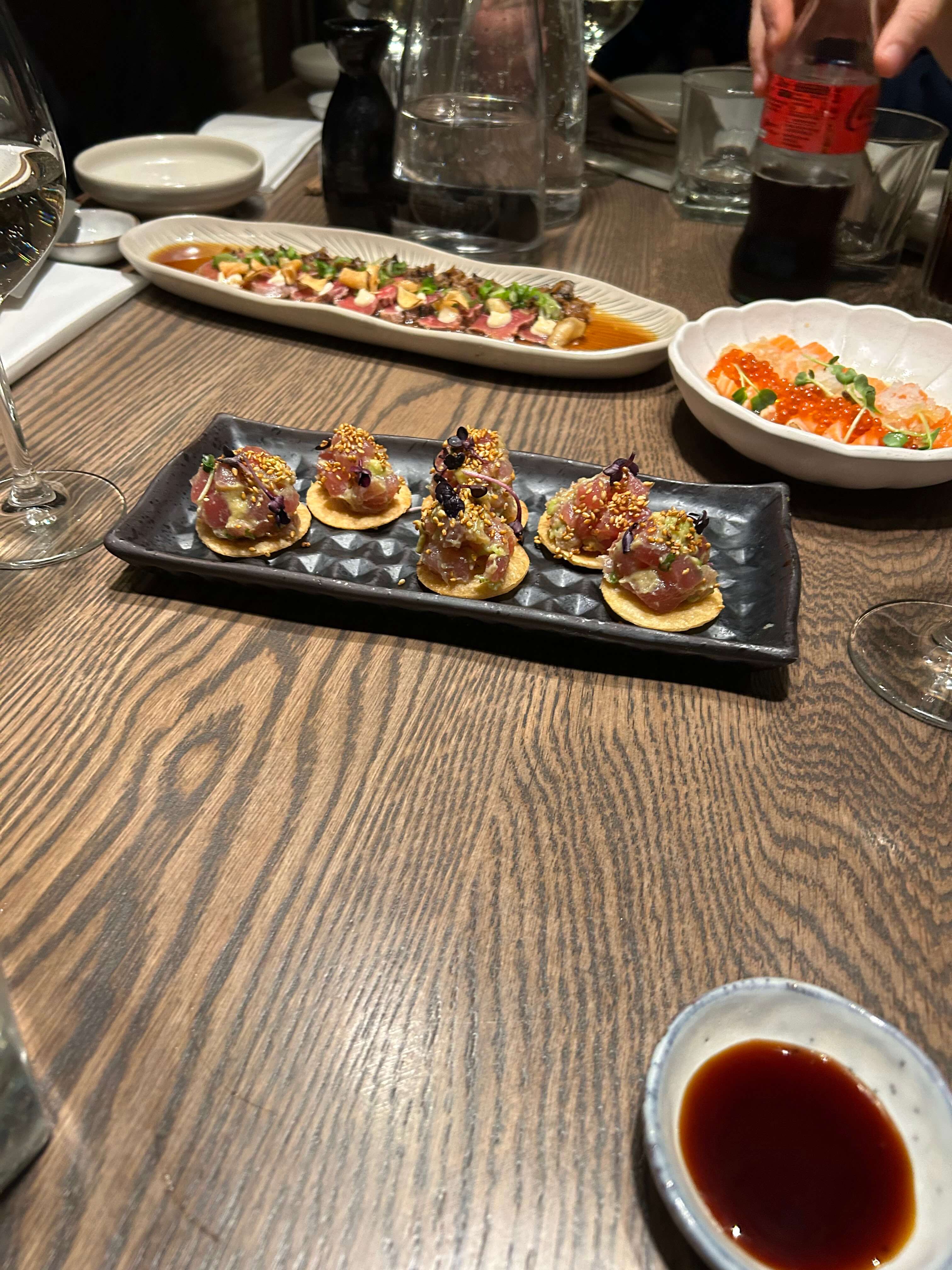 Gedeckter Tisch mit diversen asiatischen Vorspeisen, darunter Thunfisch auf Crackern und Lachskaviar, auf hölzernem Hintergrund.