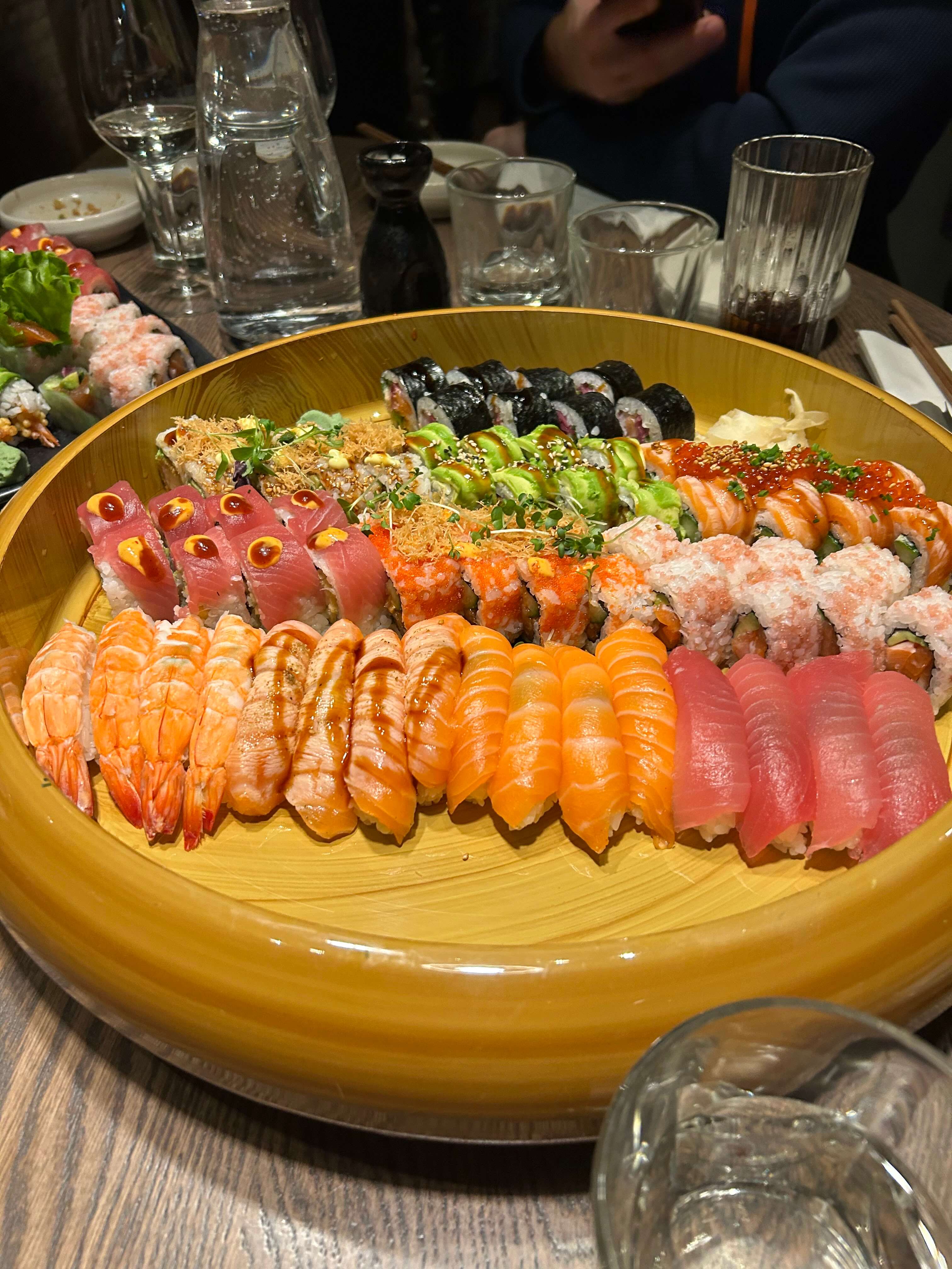 Große Sushi-Platte mit verschiedenen Sorten, darunter Nigiri und Maki, auf einem Holztisch serviert.