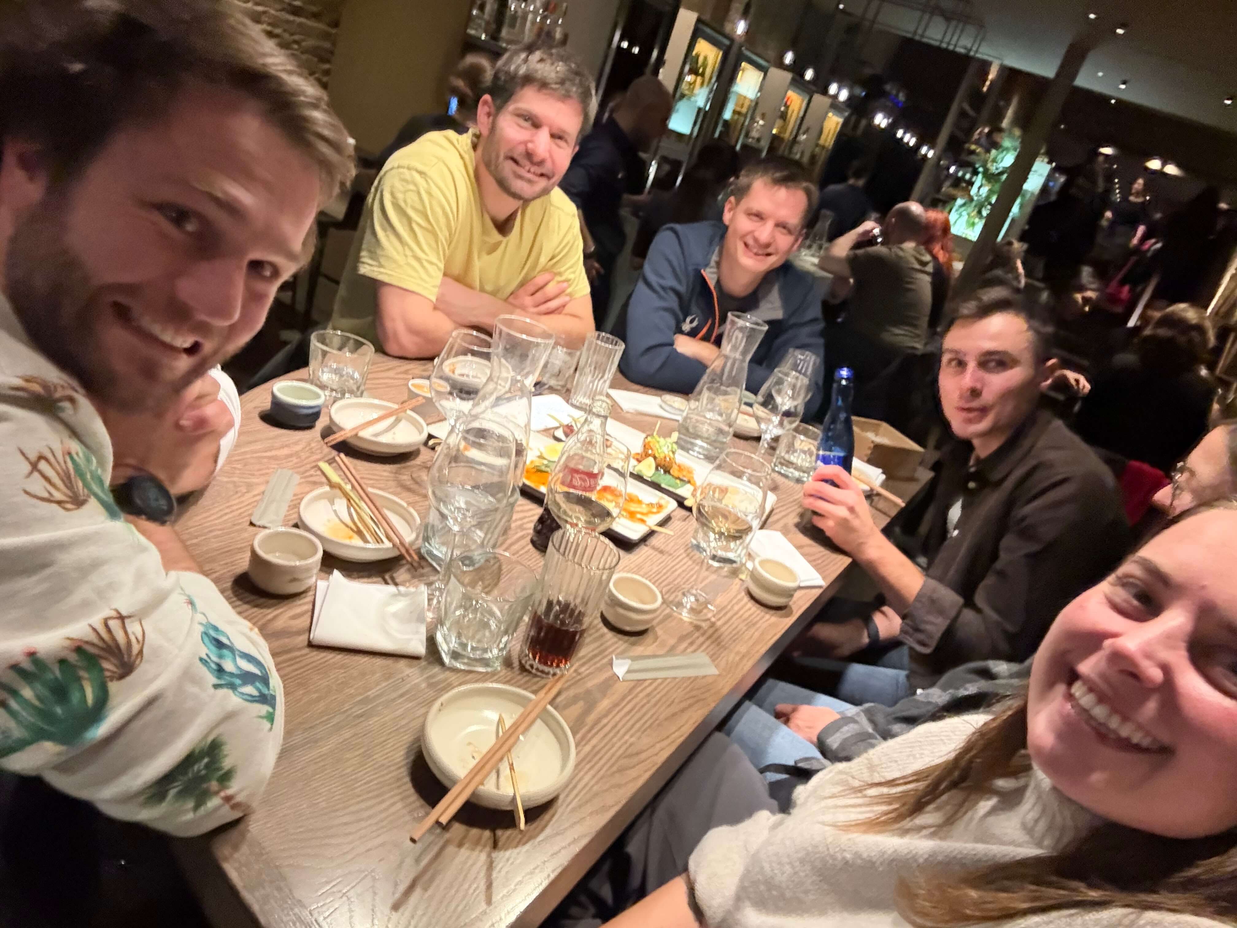Gruppe von sechs Personen lächelt bei einem Restaurantessen, Tisch mit leeren Tellern und Gläsern.