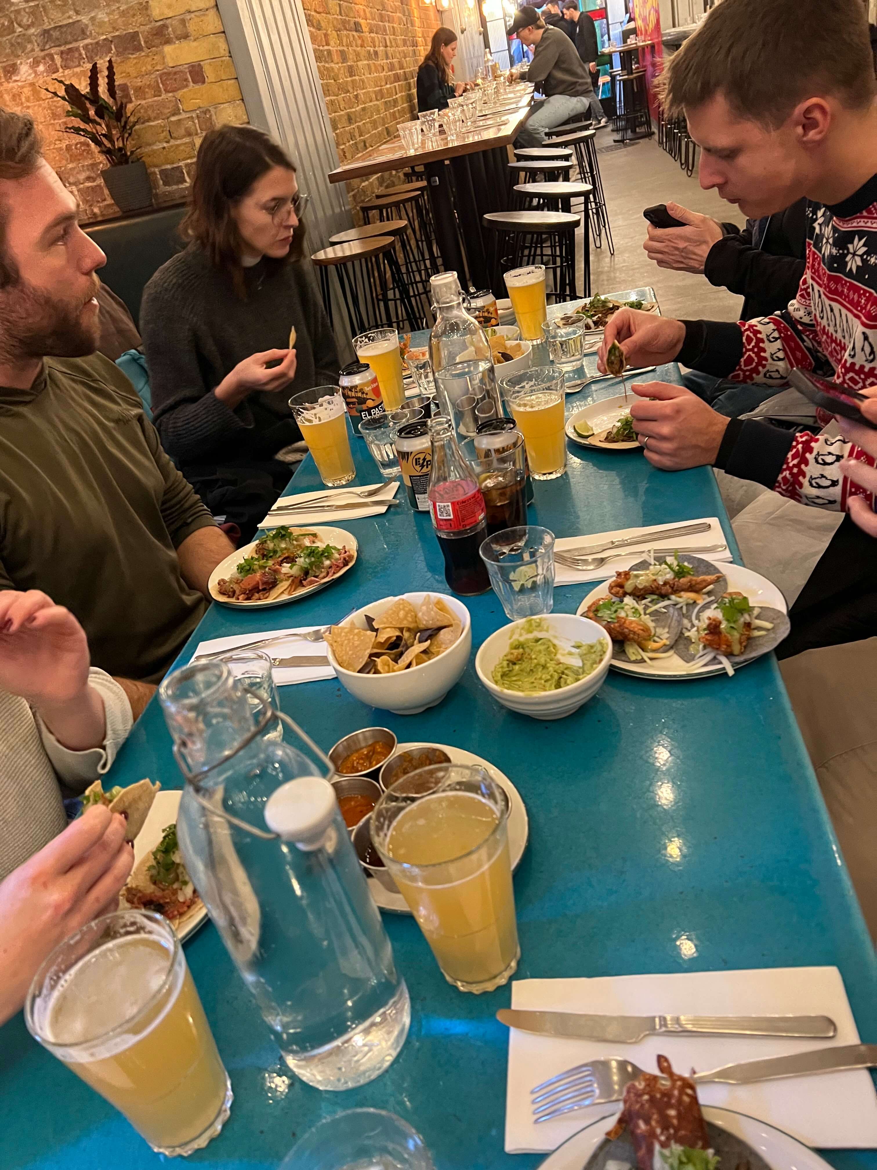 Personen essen gemeinsam an einem Tisch in einem Restaurant, mit Tacos, Getränken und Dips auf dem Tisch.