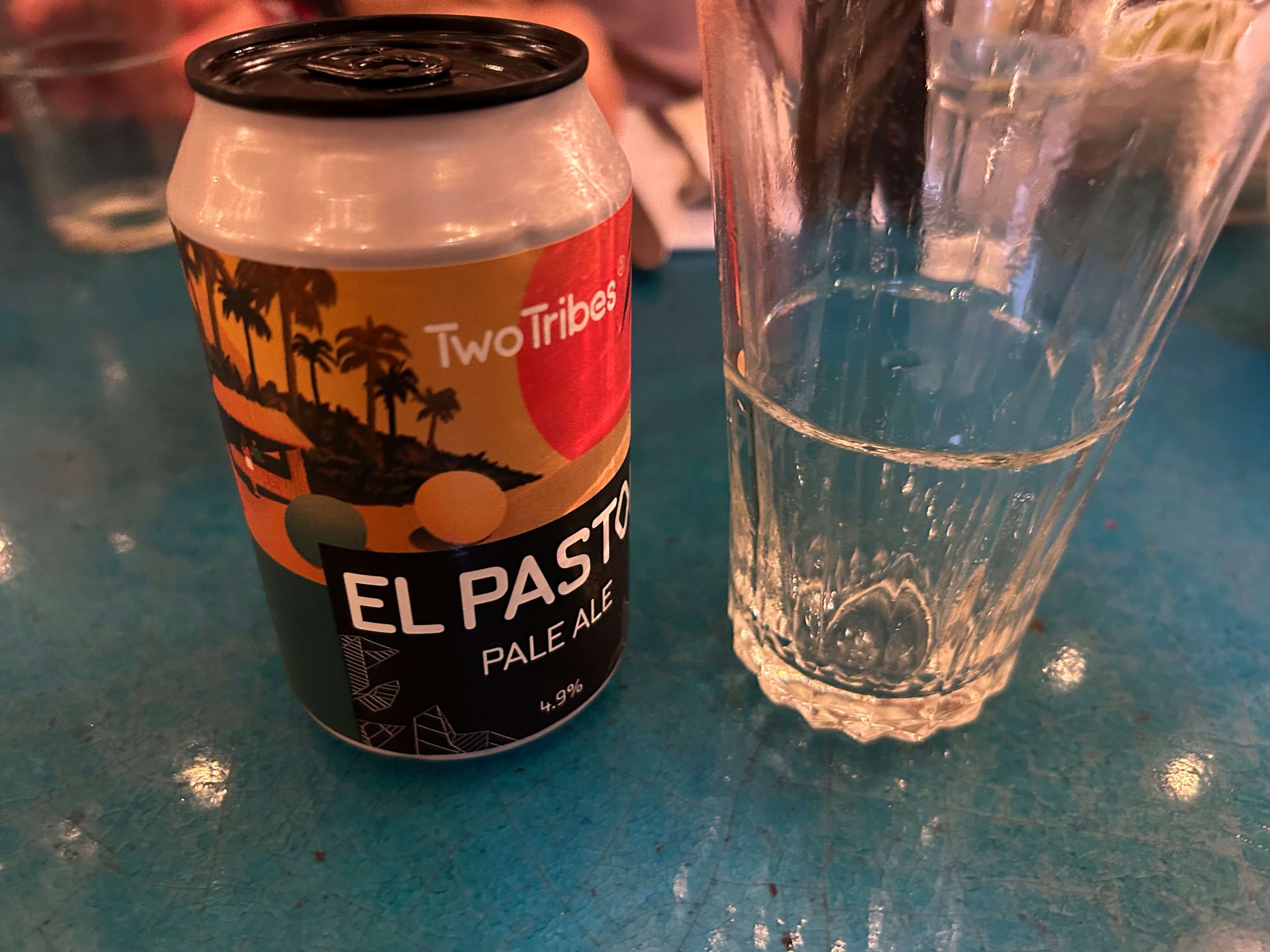 Bierdose "El Pastor Pale Ale" neben einem halbgefüllten Glas auf einem blauen Tisch.