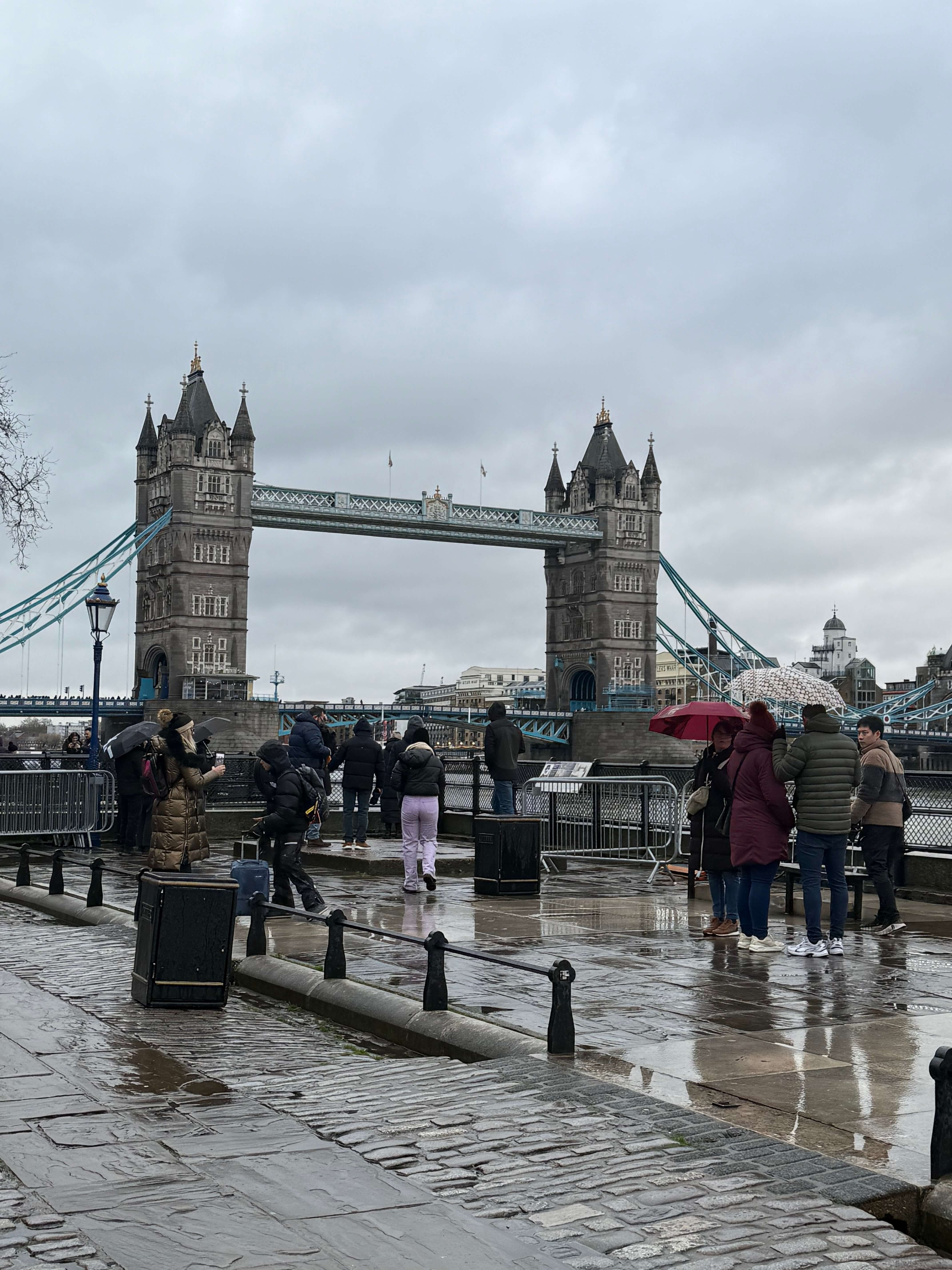 Touristen mit Regenschirmen vor der Tower Bridge in London an einem bewölkten Tag.
